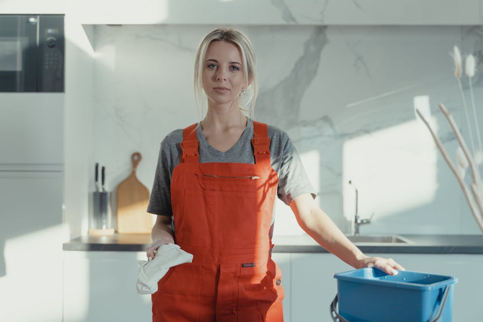 Two professional cleaners from Earls Court Cleaner are performing surface cleaning in a modern kitchen area. The female cleaner in the foreground is using a handheld vacuum or carpet cleaner on a gray